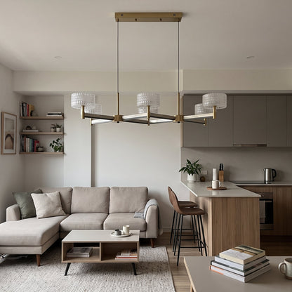 A statement 6-arm crossed pendant chandelier in brushed brass with dark accent arms, topped with six drum shades of clear textured glass.