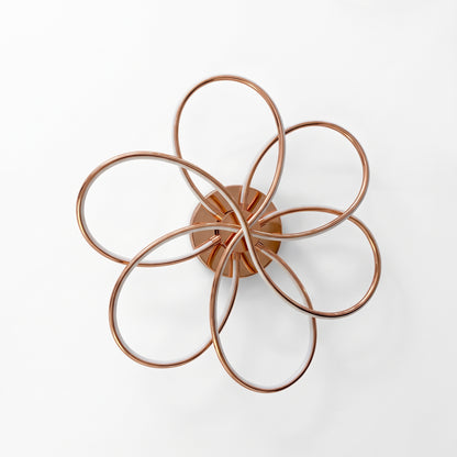 A modern LED ceiling light shaped like a flower, with six sweeping loops in a polished rose gold finish