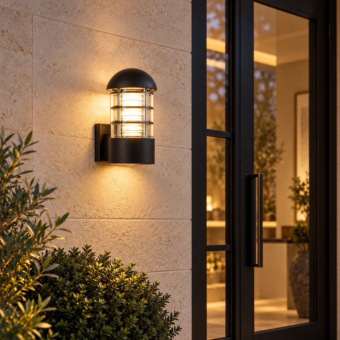 A Sunrise Lion rounded outdoor wall lantern in black aluminium and glass, with a domed cap and a ribbed cage design that casts a warm, decorative glow on the wall.