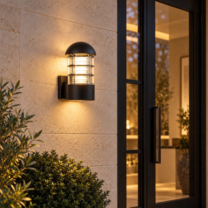 A Sunrise Lion rounded outdoor wall lantern in black aluminium and glass, with a domed cap and a ribbed cage design that casts a warm, decorative glow on the wall.
