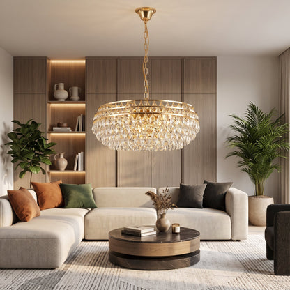 Gold crystal chandelier hanging in a modern living room with a beige sectional sofa and wooden accent wall